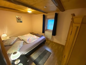 Ein kleiner, gemütlicher Raum mit einem Bett, einem Schreibtisch, einer Lampe und einem Vorhangfenster.