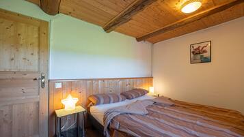 Quarto com teto de madeira, cama com roupa de cama listrada, mesa de cabeceira com abajur em formato de estrela e um quadro na parede.