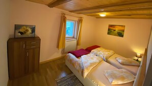 A bedroom with a wooden ceiling, a window with curtains, a bed with multiple pillows, a bedside table with a lamp, and a cabinet with a painting. - Apartment 'Maison Du Bonheur - Appartement' with Mountain View, Private Terrace and Wi-Fi (Xertigny)