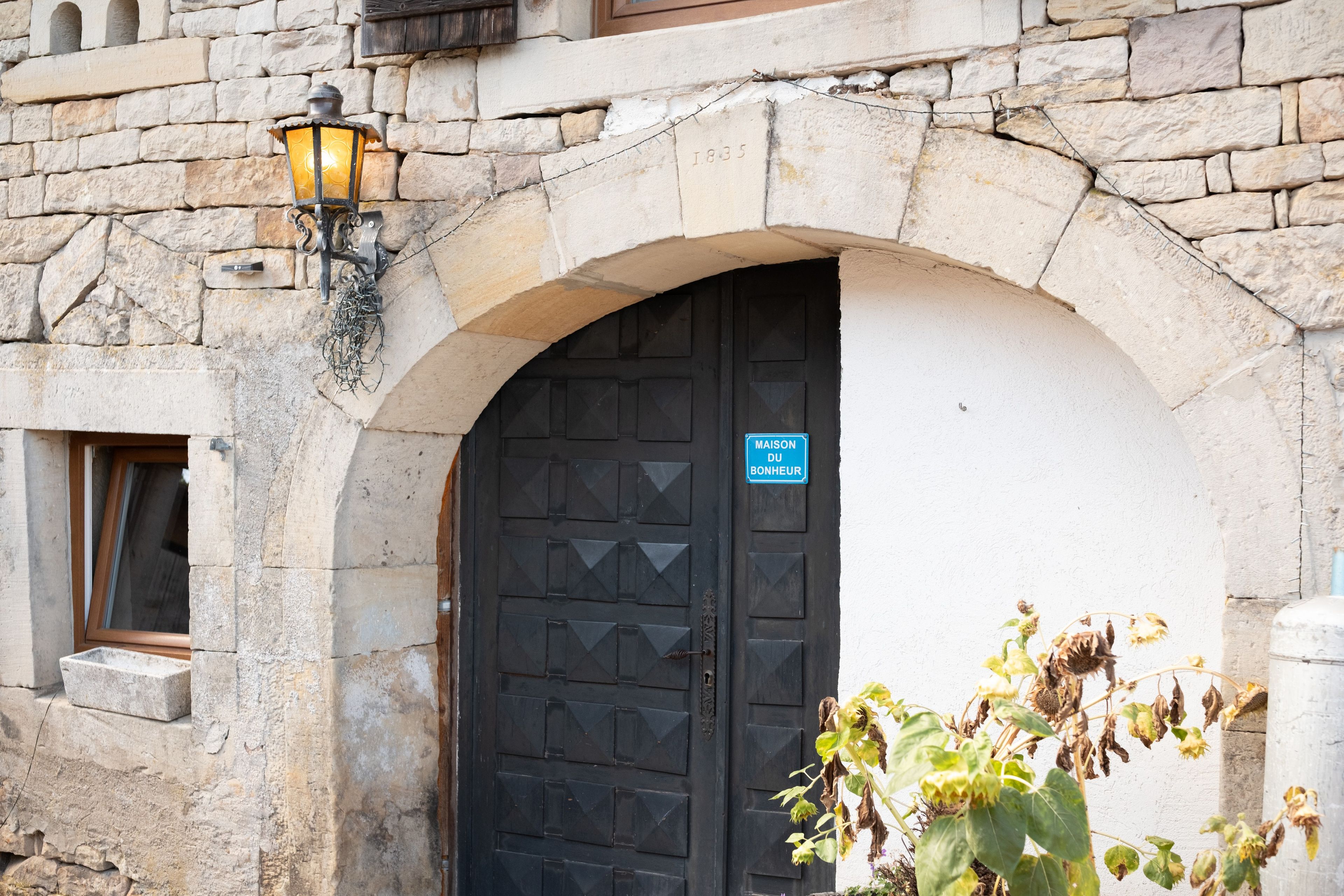 Un bâtiment en pierre avec une porte noire et une enseigne sur laquelle on peut lire : « MAISON DU BONHEUR ».