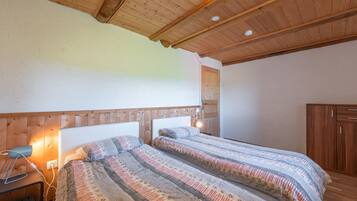 Un dormitorio con dos camas, cabeceros de madera, una mesita de noche con lámpara y un armario.