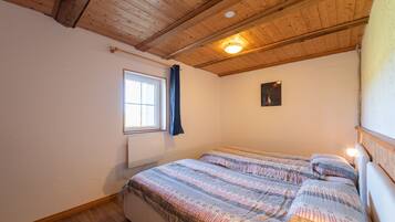 Une pièce avec un plafond en bois, une fenêtre avec des rideaux, un lit avec une literie à motifs et un tableau accroché au mur.