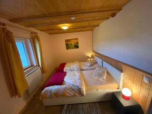 Ein Schlafzimmer mit Bett, Nachttischlampe, Fenster und einem Bild an der Wand.