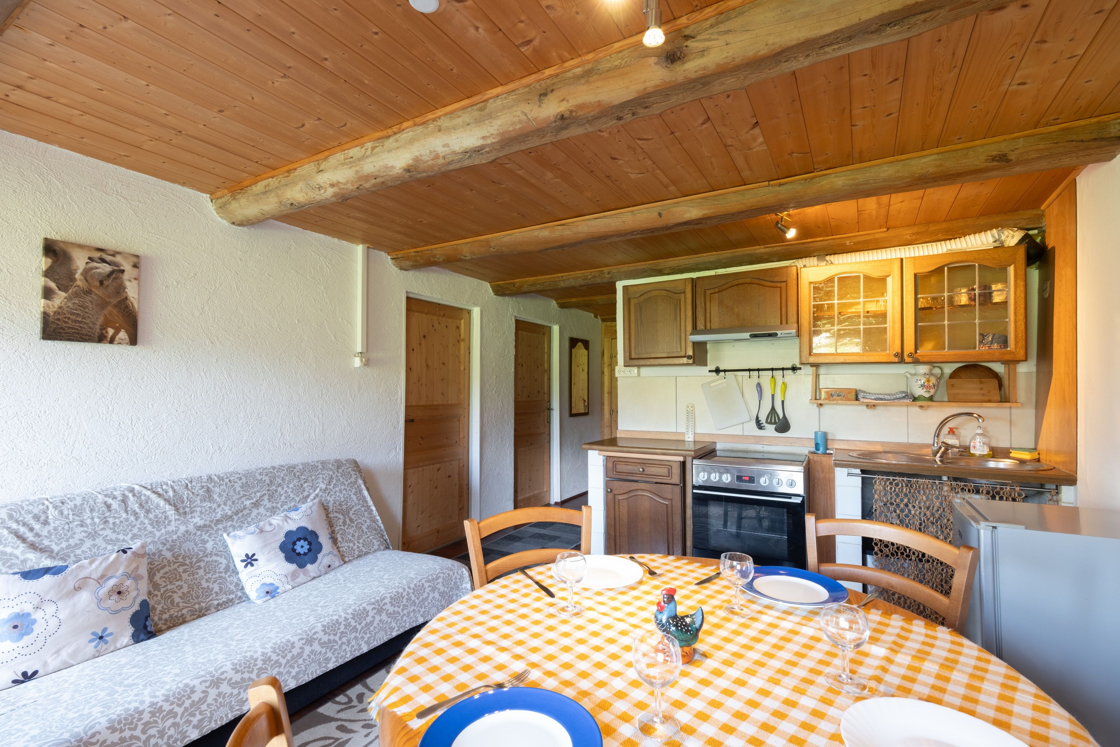 Une cuisine chaleureuse avec des meubles en bois, un poêle et un coin repas agrémenté d’une nappe à carreaux.