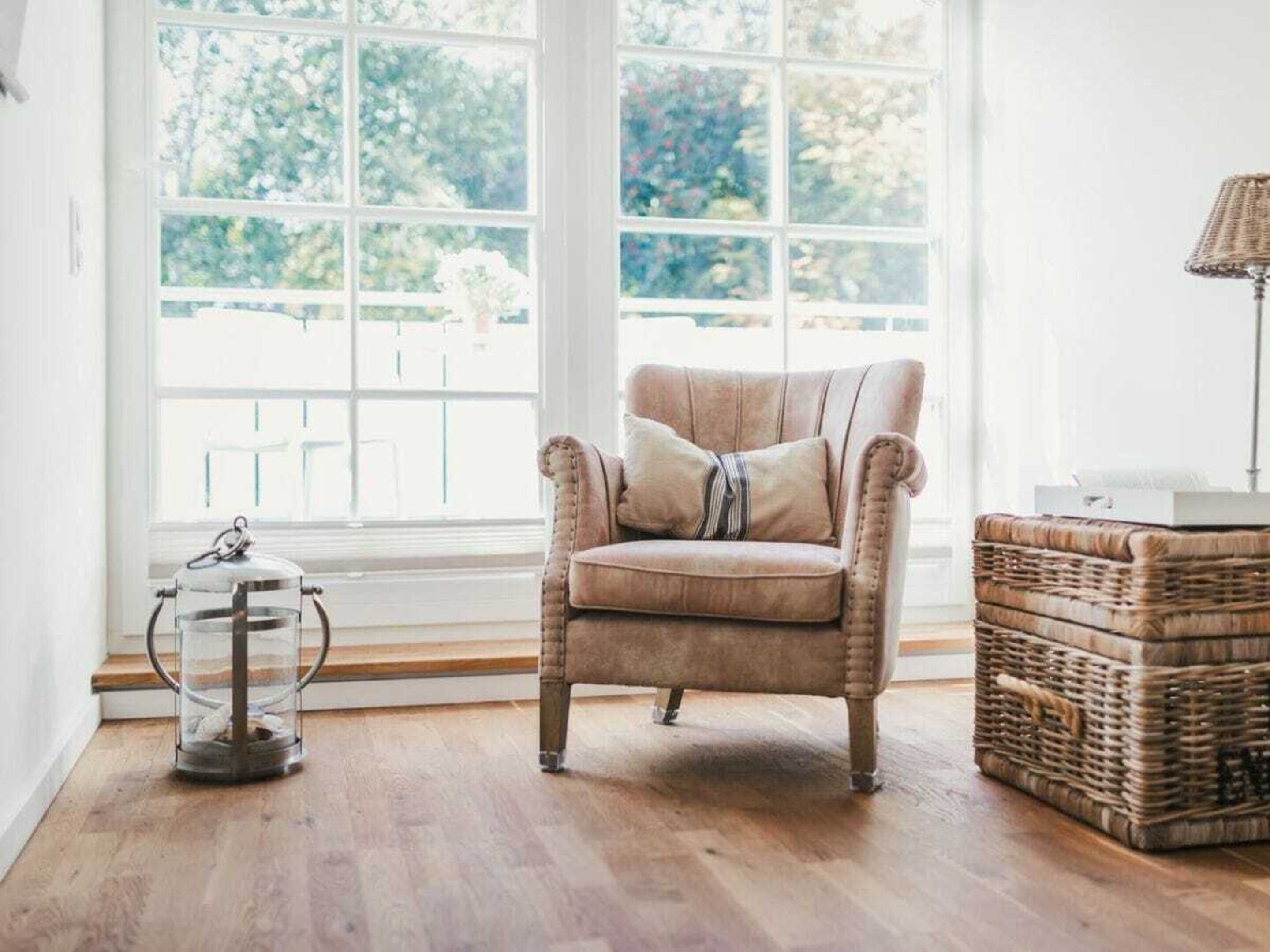 Una habitación con un ventanal grande, un sillón mullido, una cesta de mimbre y una lámpara de pie.