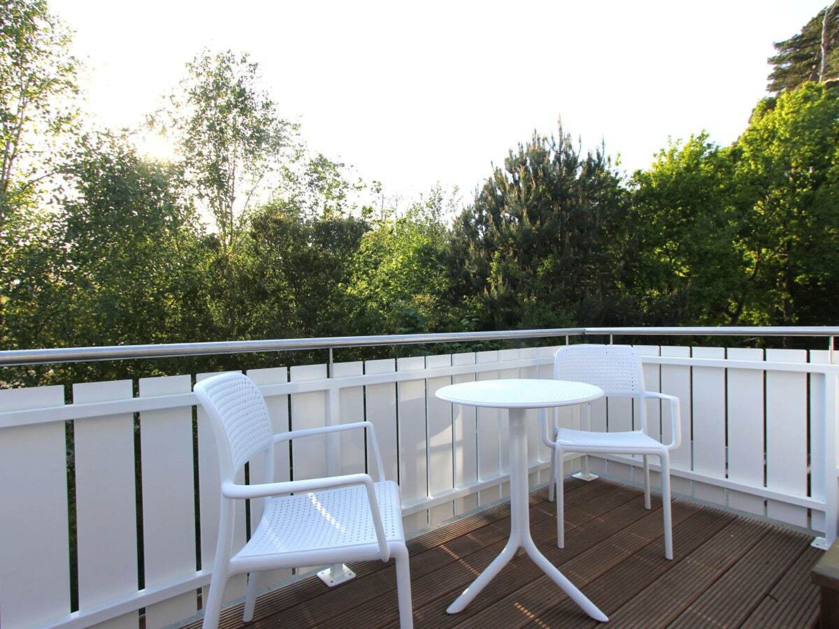 A balcony with two white chairs and a small round table, surrounded by a white railing.