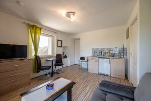 Ett kompakt bostadsutrymme med ett litet kök, en matplats och en sittgrupp med tv och soffa.