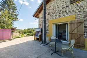 Un bâtiment en pierre avec une porte en bois, une fenêtre et un petit espace extérieur aménagé avec une table et deux chaises.