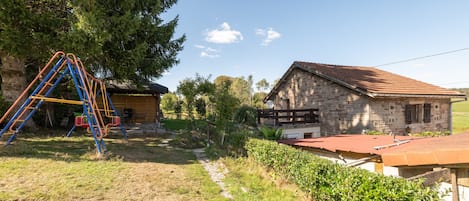 Ein rustikales Steinhaus mit rotem Ziegeldach, einer Holzterrasse und einer Schaukel im grünen Garten.