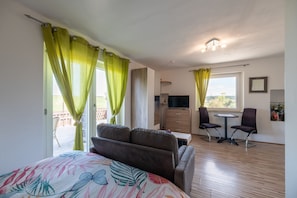 Een slaapkamer met een bed, een televisie, een bureau met twee stoelen, en een balkon met gordijnen.