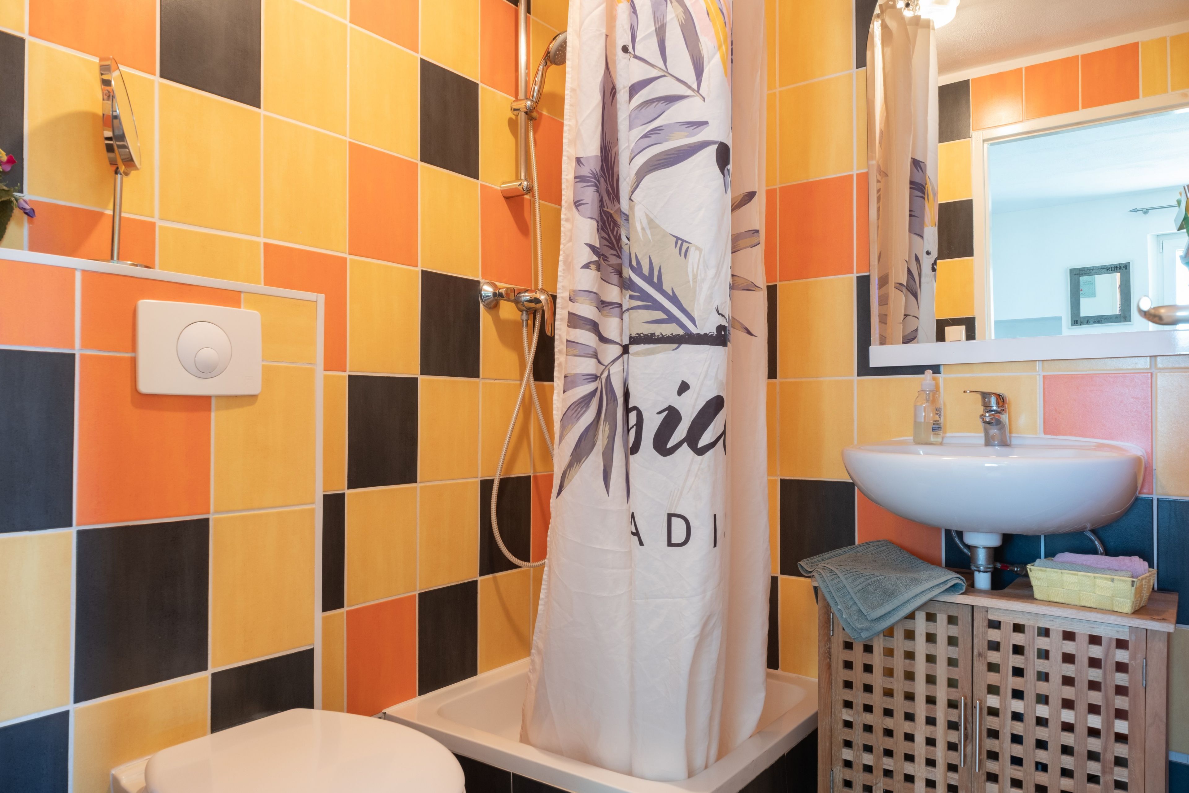 A bathroom with a tiled wall, a shower curtain, a sink, and a toilet.