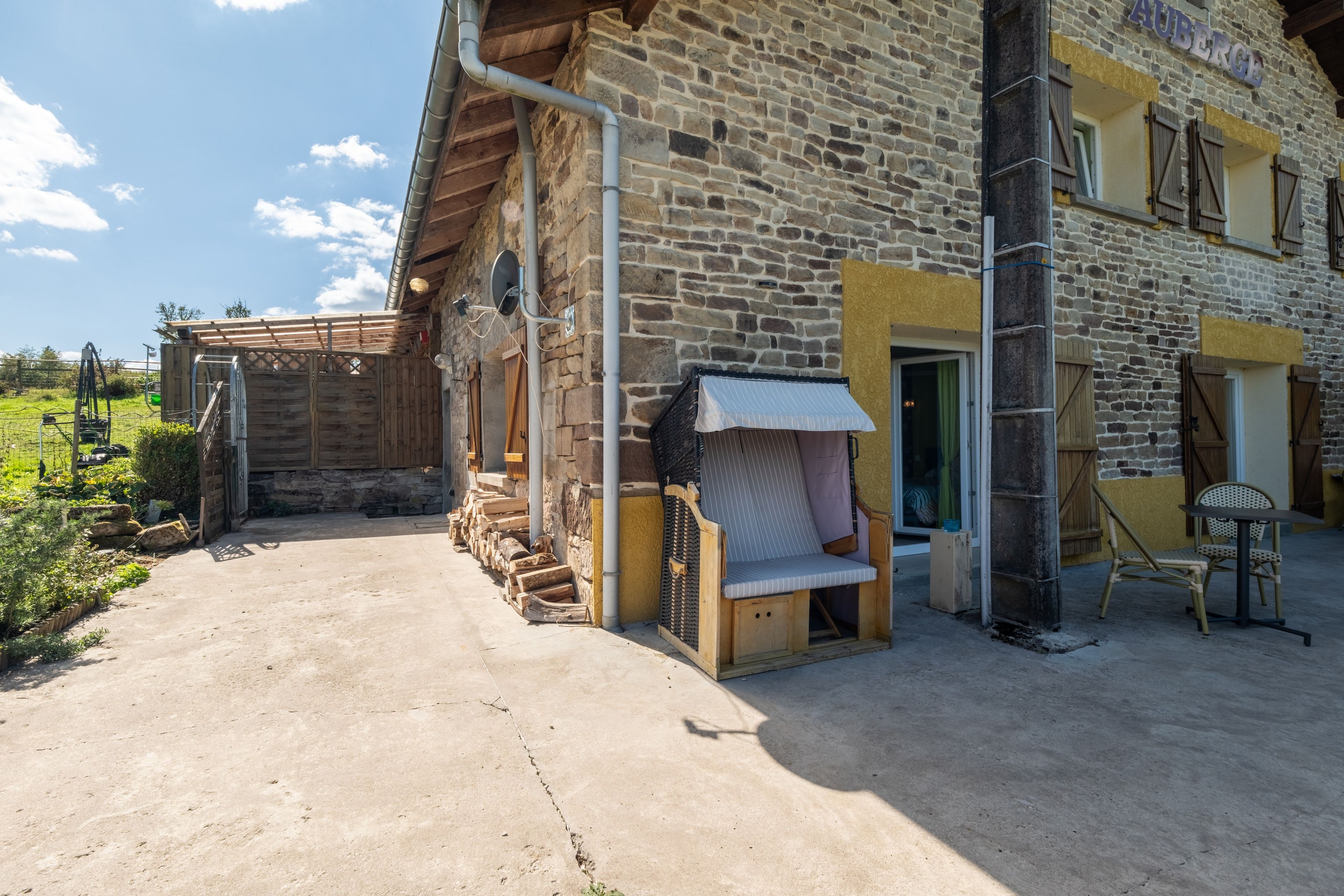 Un bâtiment en pierre doté d’un porche en bois, d’un espace de repos couvert et d’une allée pavée.