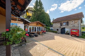 A courtyard with a wooden building, a stone building, and a red vehicle parked outside. - Guest Room "Chambre Double - Côté Jardin": Mountain View, Private Terrace & Wi-Fi (Xertigny)