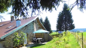 Une maison en pierre avec un toit en tuiles, une terrasse en bois et une petite table entourée de chaises.