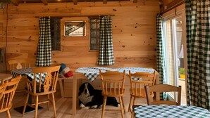 A wooden cabin interior with a dining area, checkered tablecloths, and a dog lying on the floor. - Guest Room "Double Room - Petit moulin" with Mountain View, Shared Terrace and Wi-Fi (Xertigny)