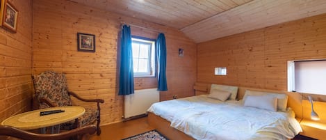 Una habitación de cabaña de madera con una cama, una silla, una mesita y un ventanal con cortinas.