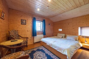 Ein Zimmer in einer Holzhütte mit einem Bett, einem Sessel, einem kleinen Tisch und einem Fenster mit Vorhängen.