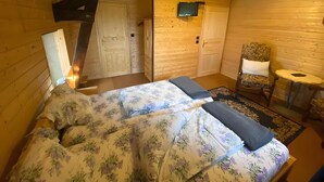 A wooden cabin bedroom with a bed, a chair, a small table, and a television. - Guest Room "Double Room - Petit moulin" with Mountain View, Shared Terrace and Wi-Fi (Xertigny)