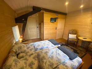 Een slaapkamer in een houten blokhut, met een bed, een stoel, een tafeltje en een televisie.
