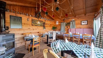 A rustic wooden interior with tables and chairs, a fireplace, and a menu board.