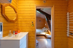 A wooden cabin interior with a bathroom, a bed, and a small table.