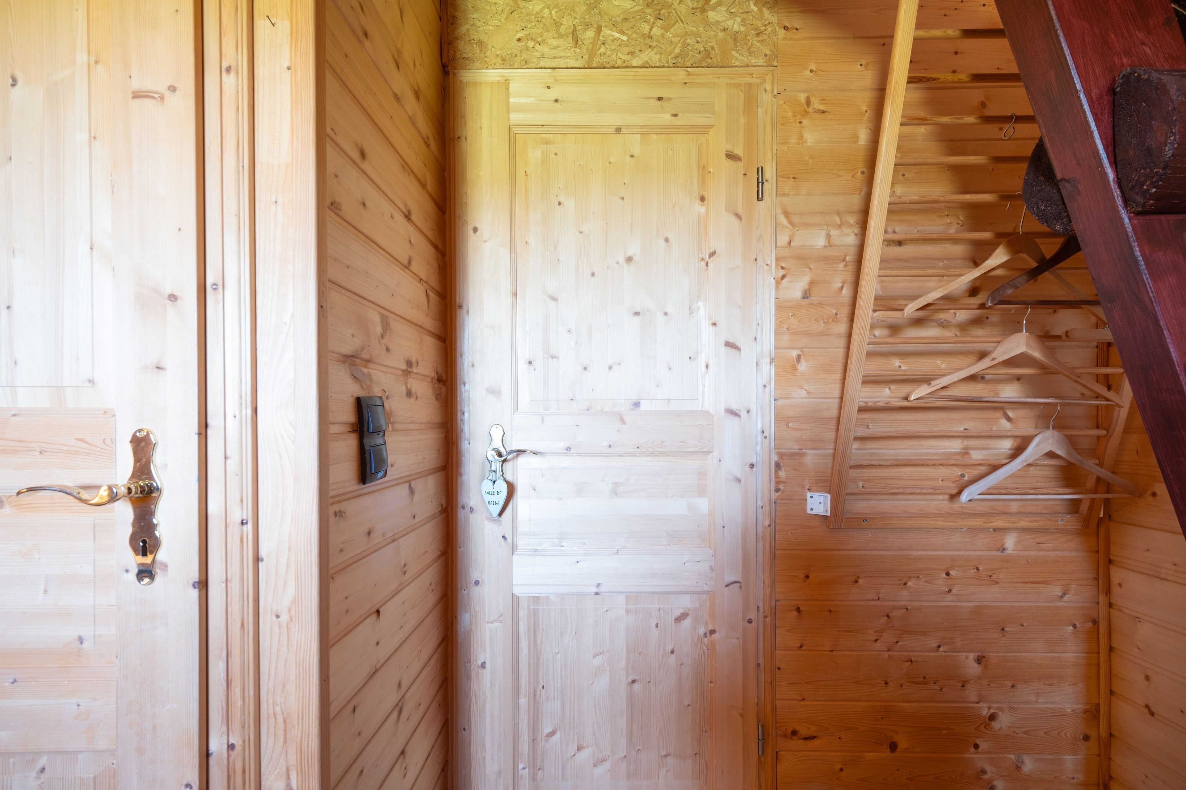 Een houten interieur met een deur, een kapstok en een ophangende jas.
