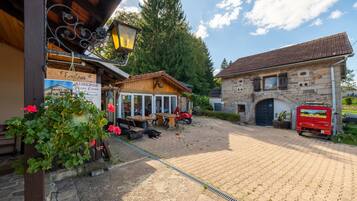 A courtyard with a wooden building, a stone building, and a red vehicle parked outside.