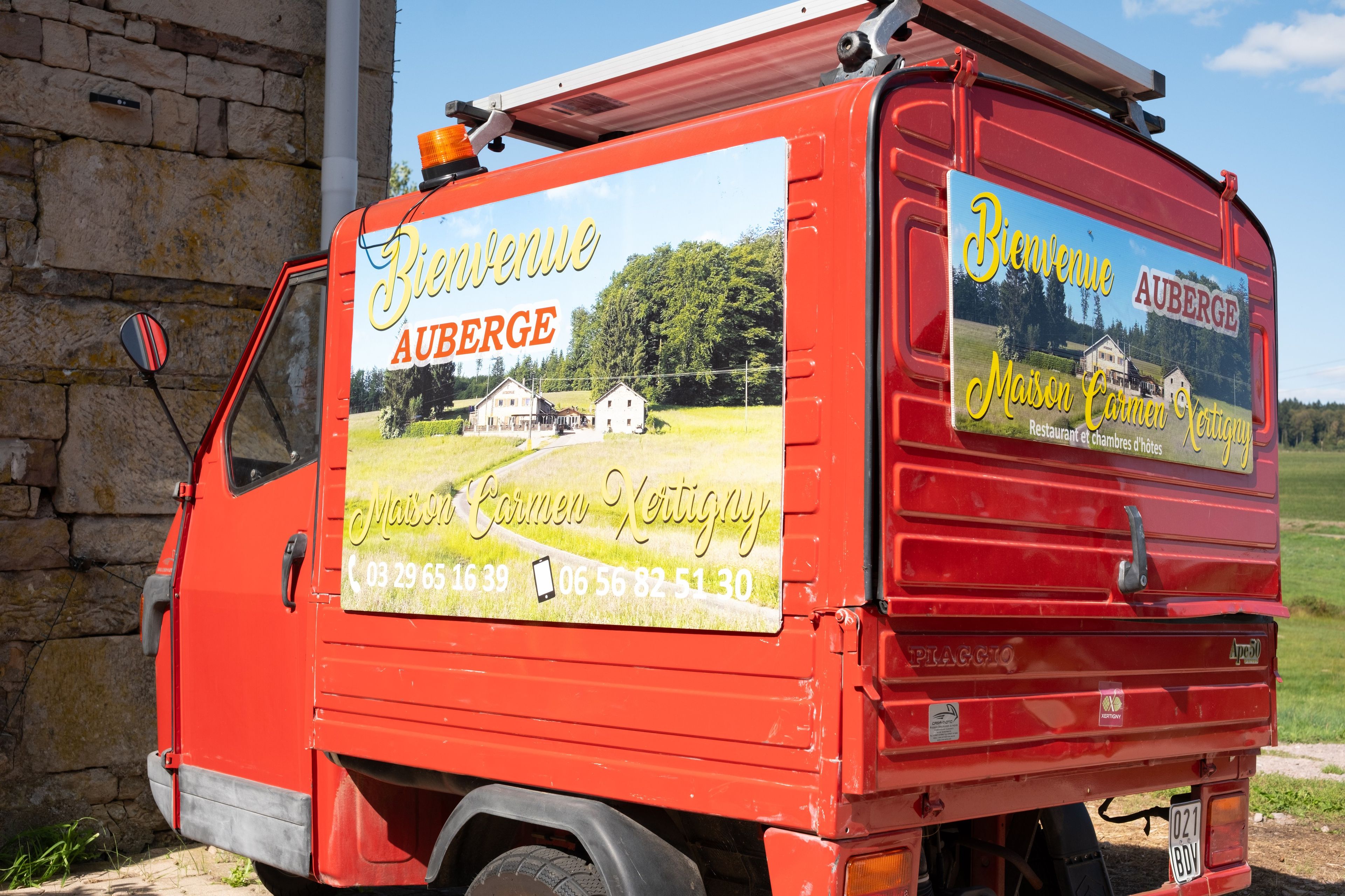 A red delivery truck with advertisements for Maison Carmen Vertigny and Auberge, featuring contact numbers and a scenic image of a house.