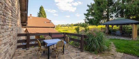 A patio with a table and chairs, a wooden fence, and a view of a field and trees.