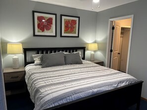 Een slaapkamer met een bed, twee bedlampen, een deur en twee florale kunstwerken in lijsten aan de muur.