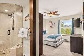 Ein Hotelzimmer mit Dusche, einem Bett mit Blick, einem Deckenventilator und Kunstwerken an den Wänden.