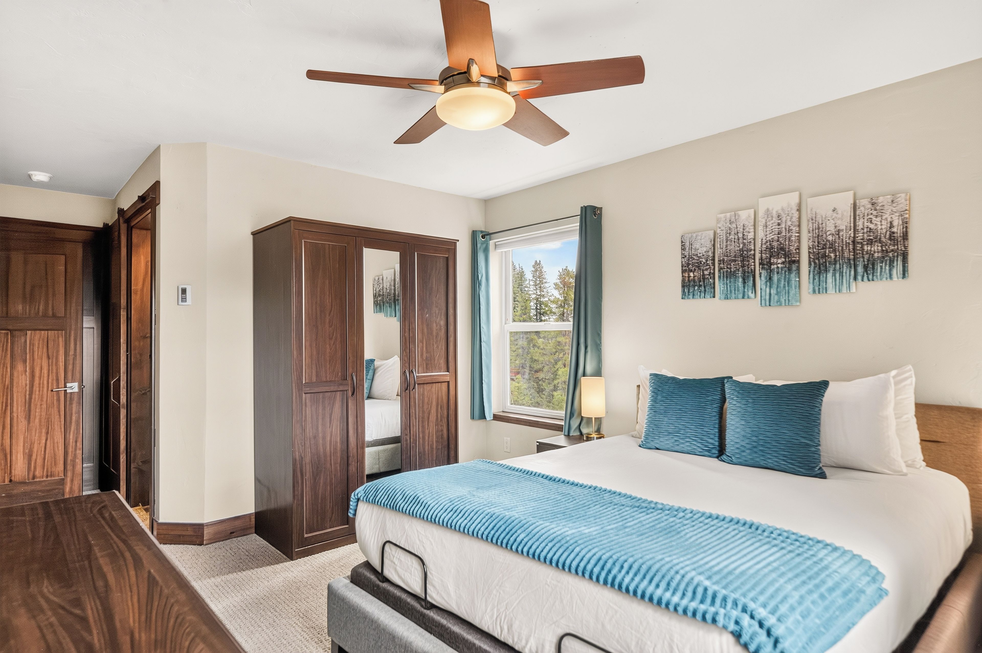 A bedroom with a bed, a wardrobe, a ceiling fan, a window with curtains, and wall art.