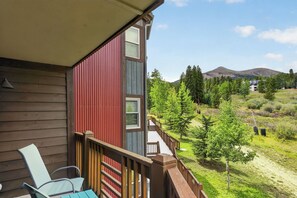 Ein Holzgebäude mit Balkon, das auf eine Wiese mit Bäumen und einen Berg im Hintergrund blickt.