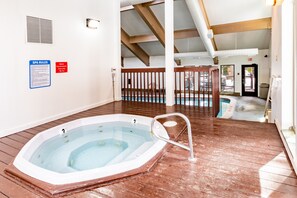 Un bain à remous dans une pièce dotée d’un plancher en bois, d’un plafond avec des poutres apparentes et d’un panneau indiquant les règles du spa.