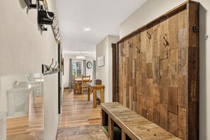 Ein Flur mit einer Holzbank, einem Schrank mit Haken und einem Essbereich mit Stühlen und Tisch.