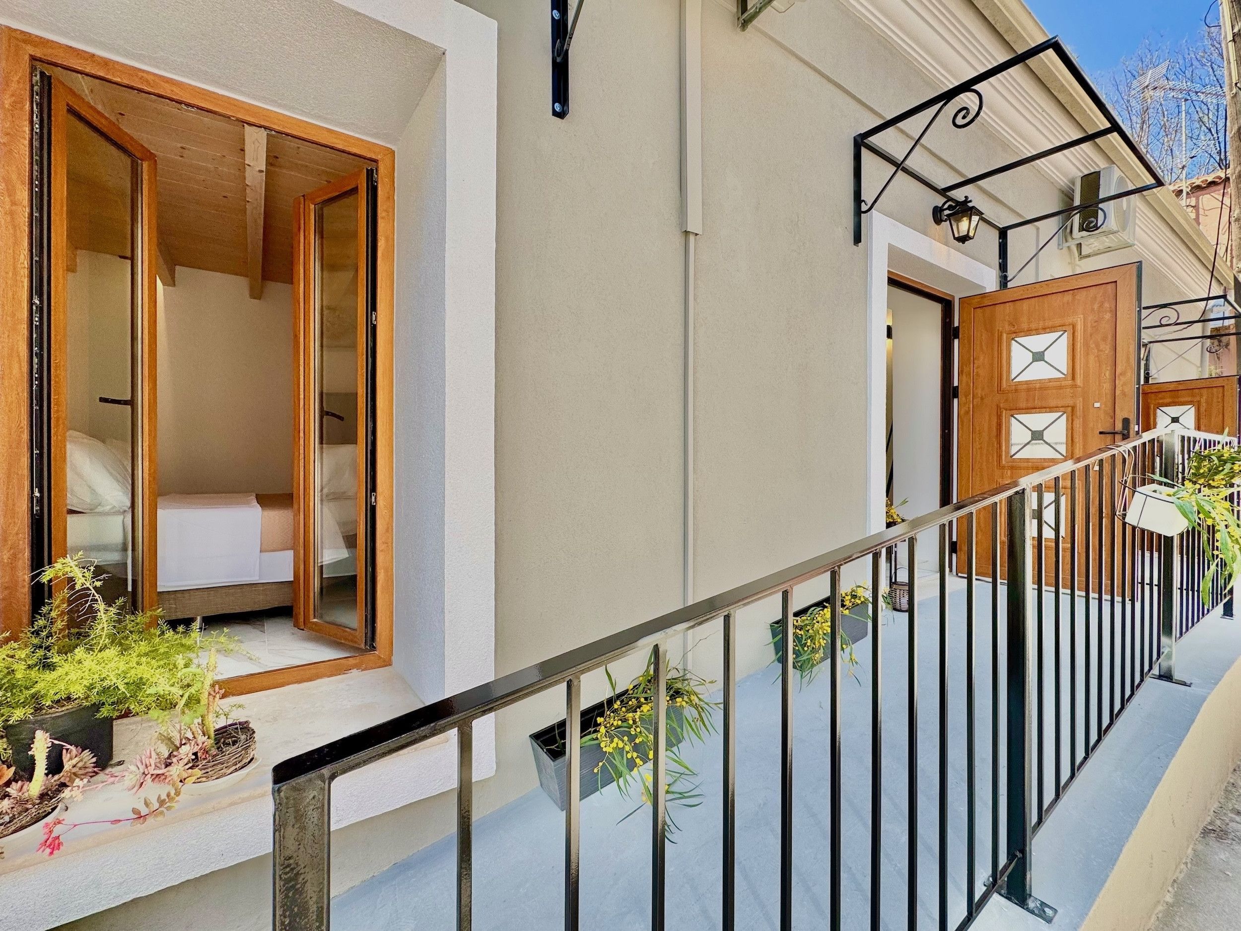Una habitación de hotel con una puerta de madera, un balcón con barandilla de metal y plantas en macetas.