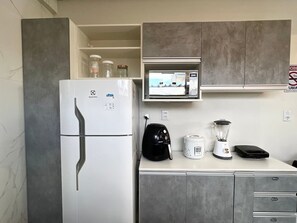 Eine Küche mit einem weißen Kühlschrank, einer Kaffeemaschine, einem Mixer und einer Mikrowelle.