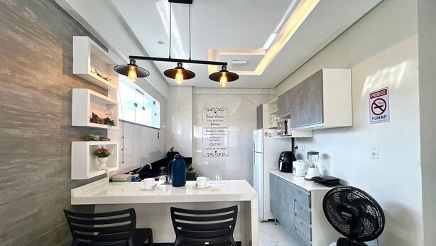 Een compacte keuken met een centraal eiland, zwarte stoelen, een inbouwoven en een ventilator aan de muur.