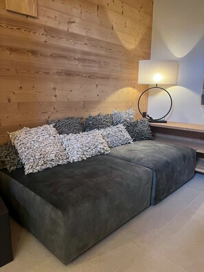 Ein modernes Wohnzimmer mit einer Eckcouch, einem runden Tisch mit Lampe und einer Holzwand.
