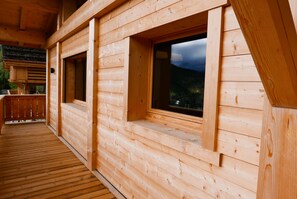 Une cabane en bois dotée d’une terrasse et de grandes fenêtres.
