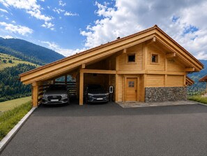 Eine Holzchalet mit zwei Autos auf der Auffahrt, vor einer Bergkulisse.