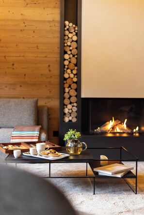 Un salon chaleureux avec une cheminée, une table basse, un canapé et un plateau contenant des biscuits et une tasse.