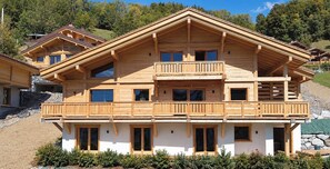 Un chalet en bois à plusieurs étages, doté de balcons, de grandes fenêtres et de fondations en pierre.
