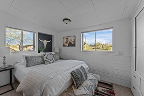 A bedroom with a large bed, two windows, and artwork on the walls. - Private Western Desert Retreat Horses Welcome (Maricopa County)