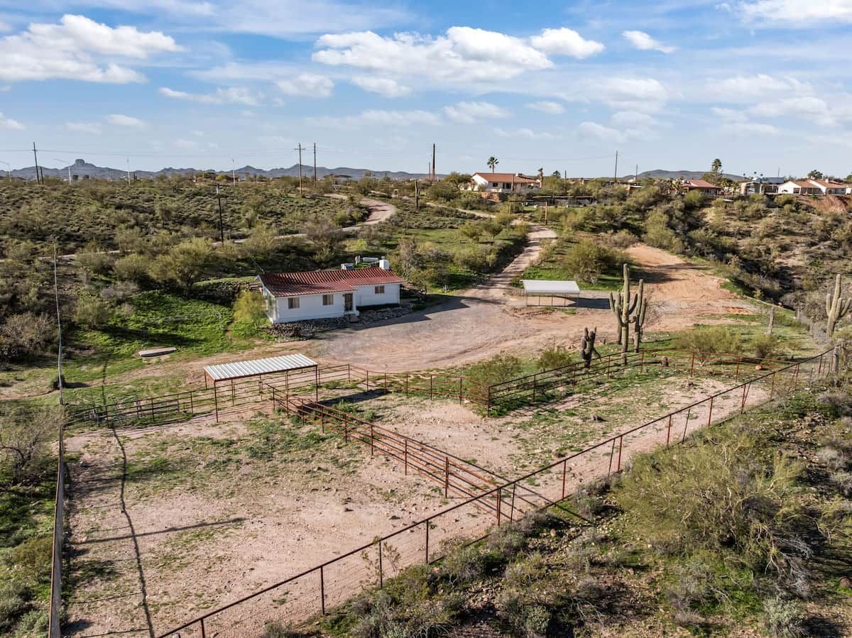 A rural landscape with a white house, a fenced area, and sparse vegetation.