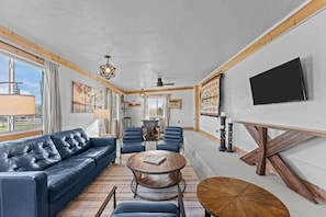 A spacious living room with a leather sofa, round coffee table, and blue chairs. A flat-screen TV is mounted on the wall, and there are large windows providing natural light. - Private Western Desert Retreat Horses Welcome (Maricopa County)
