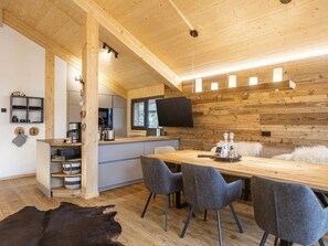 A modern kitchen with wooden walls, a dining area with grey chairs, and a large flat-screen TV mounted on the wall. - Superior Chalet # 24 With Sauna & Hot Tub (Stadl-Predlitz)