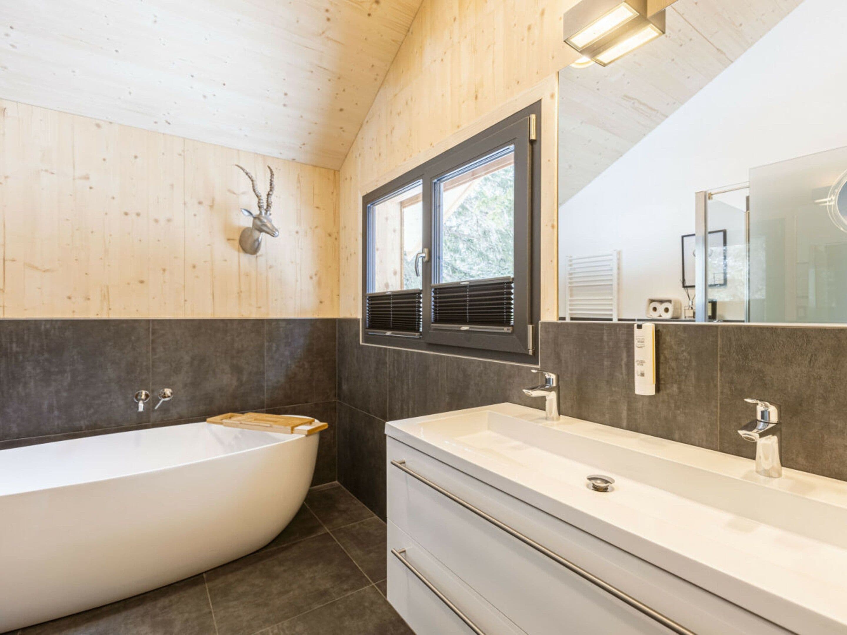 Ein modernes Badezimmer mit einer freistehenden Badewanne, einem großen Spiegel und einem Fenster mit Jalousien.