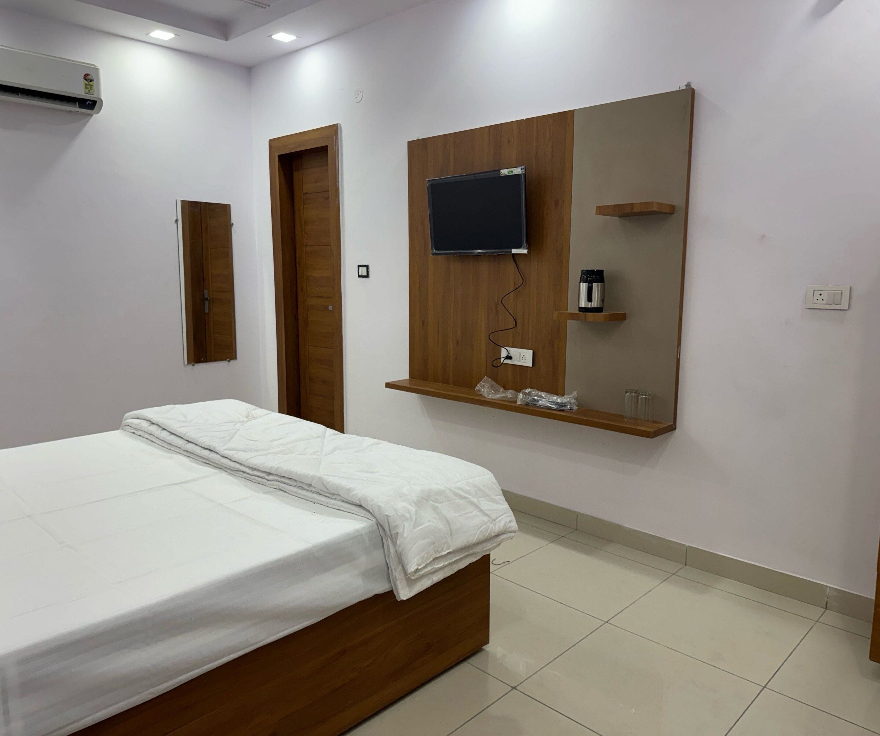 Quarto com cama, televisão fixada na parede, guarda-roupa de madeira e espelho.
