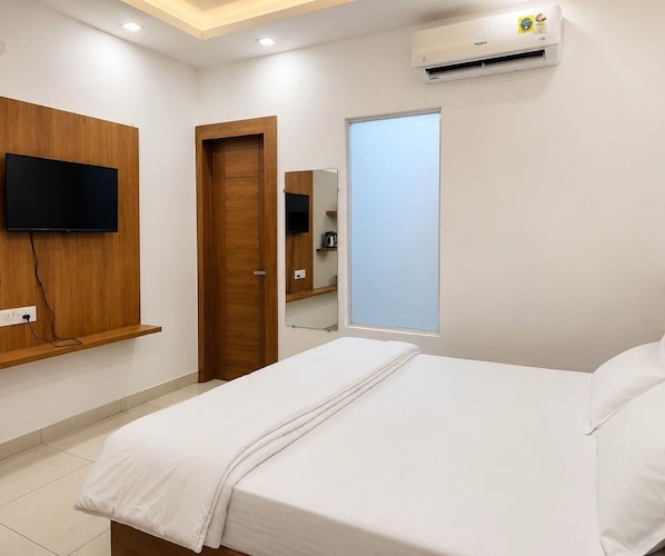 A hotel room with a bed, a television mounted on the wall, a door, and an air conditioning unit. - Deluxe Room Hotel Welnis Inn (Amritsar)
